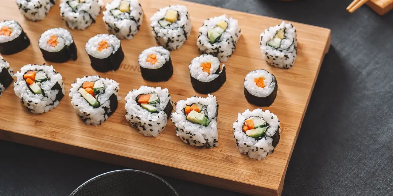 Selbstgemachtes Sushi mit Karotten und Gurken auf einem Holzbrett. So einfach kann Sushi selber machen sein!