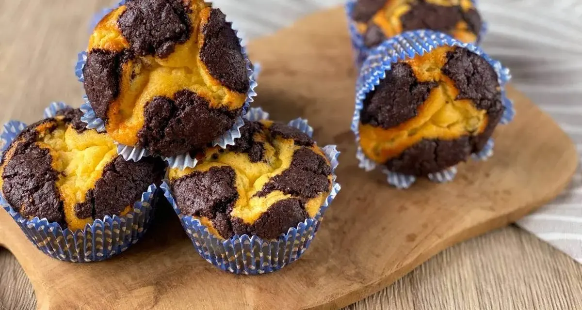 Zupfkuchen Muffins mit Marmormuster aus dunklem Schoko- und hellem Teig in blauen Papierförmchen auf einem Holzbrett.