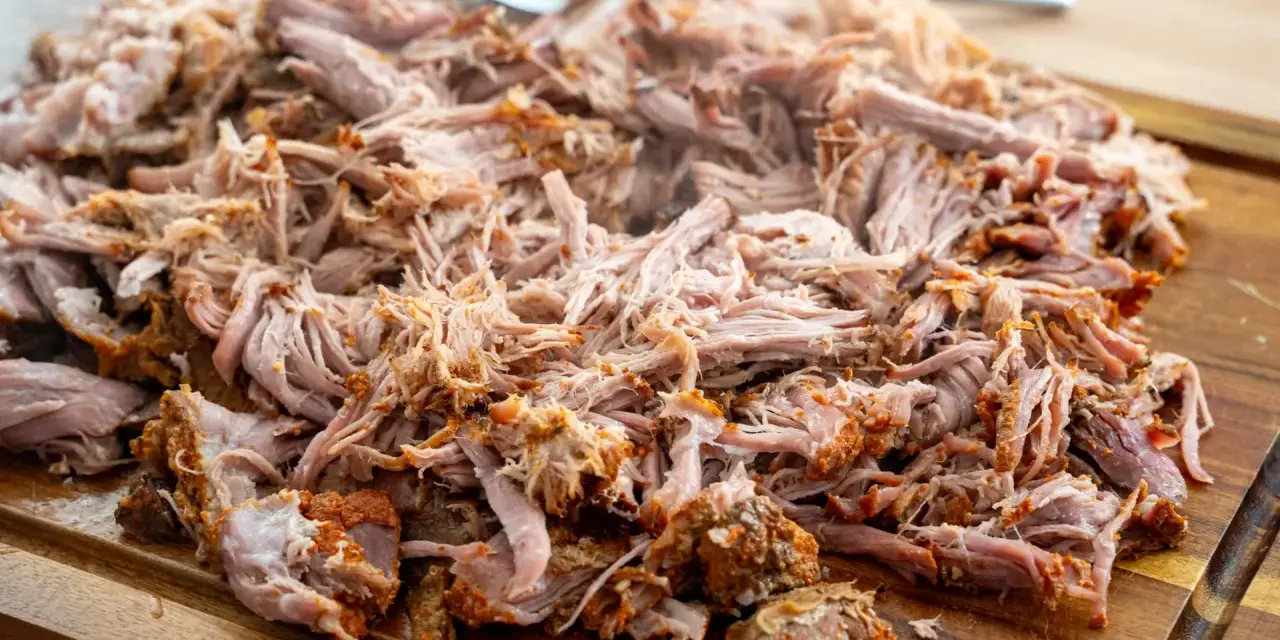 Saftiges pulled pork, zart zerfallen, liegt auf einem Holzbrett. Eine Gabel liegt bereit, um das Fleisch zu servieren.