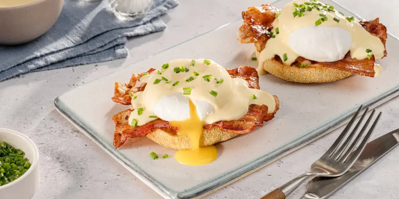 Zwei köstliche Eggs Benedict auf einem Teller, mit flüssigem Eigelb und garniert mit Schnittlauch.