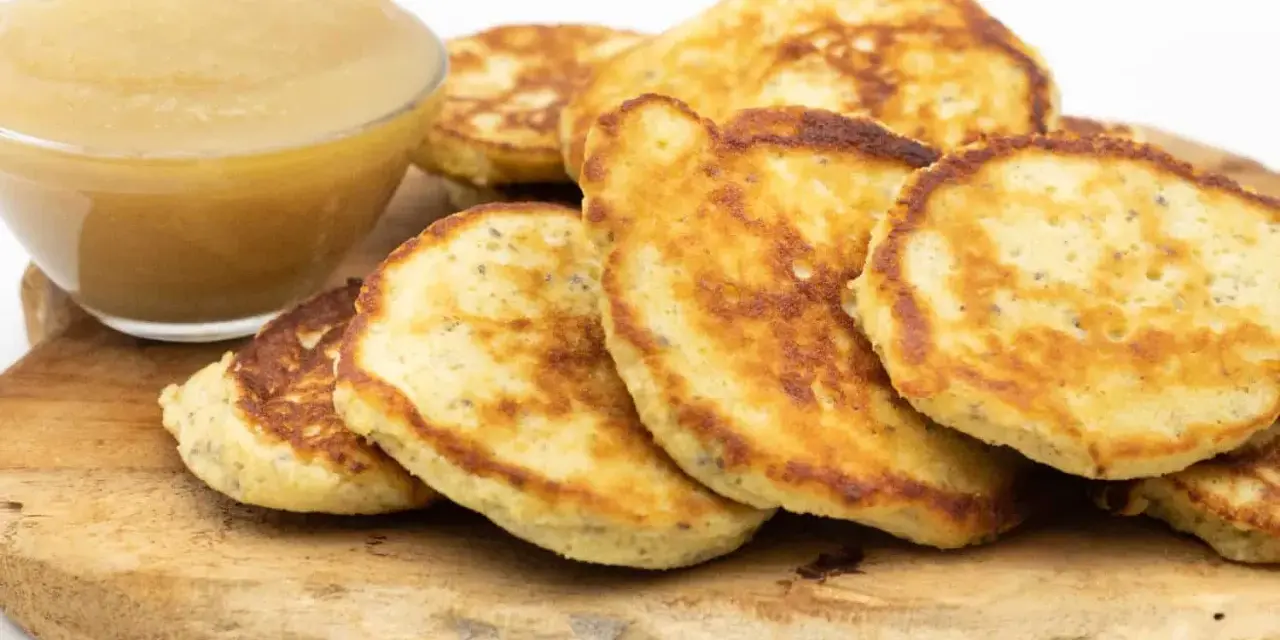 Goldbraune Quarkkeulchen ohne Kartoffeln, serviert mit Apfelmus auf einem Holzbrett.