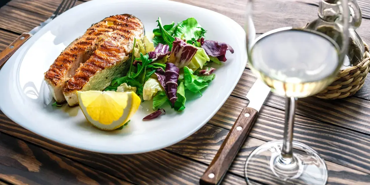 Gegrilltes Lachsfilet mit Salat und Zitrone, dazu ein Glas Weißwein, der den Riesling Geschmack unterstreicht.