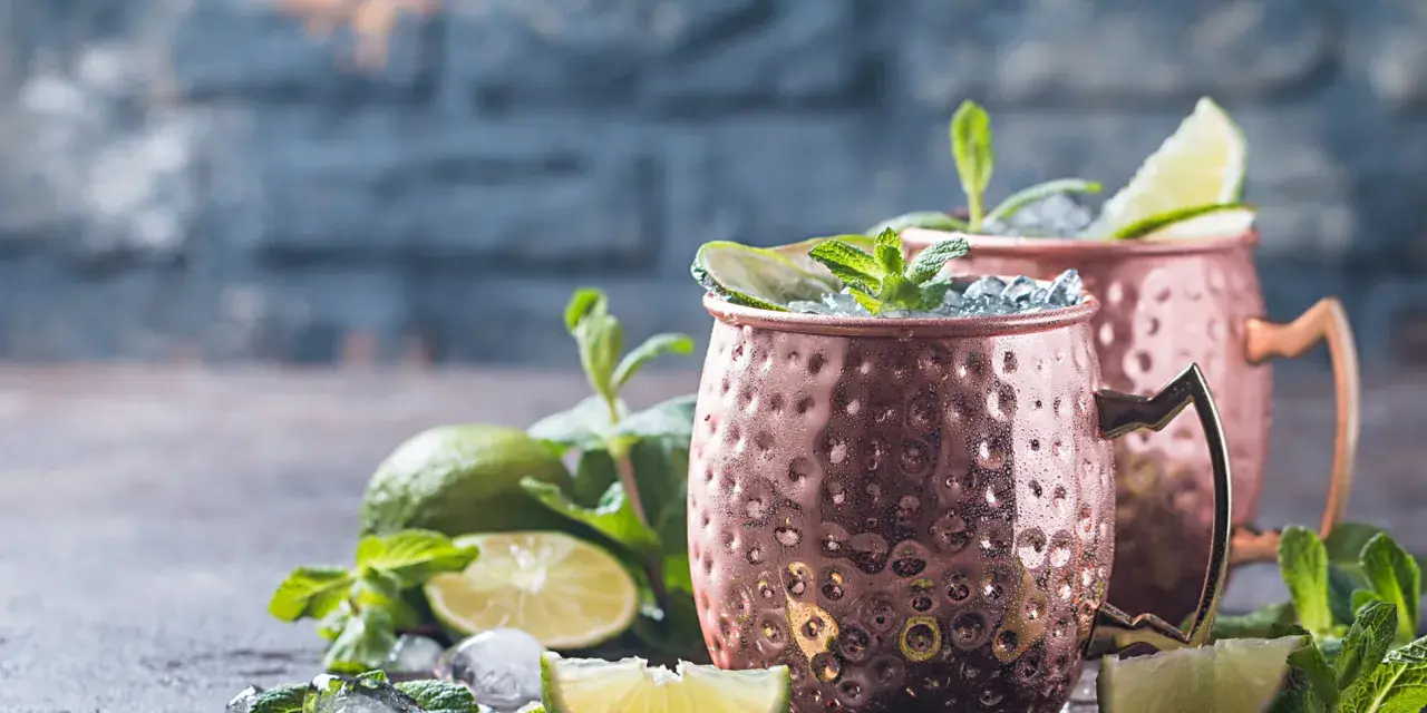 Zwei eisgekühlte Kupferbecher mit einem erfrischenden alkoholfreien Ginger Beer Cocktail, garniert mit Limette und Minze.
