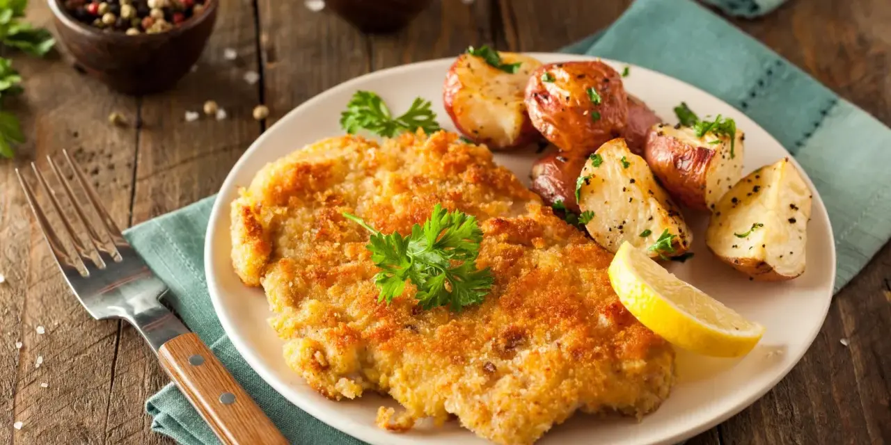 Goldbraunes Schnitzel, perfekt paniert, mit Rosmarinkartoffeln und Zitrone. Die richtige **Schnitzel panieren Reihenfolge** macht's möglich!