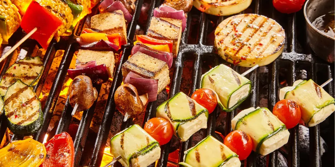 Bunte Spieße mit Tofu, Zucchini, Tomaten und Mais werden auf einem Grill zubereitet. Ein Genuss für vegetarisches Grillen!
