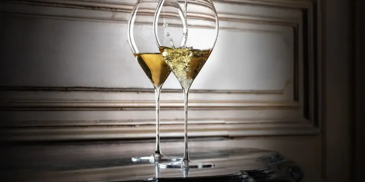 Zwei elegante Gläser, eines wird mit Champagner gefüllt. So trinkt man Champagner stilvoll.