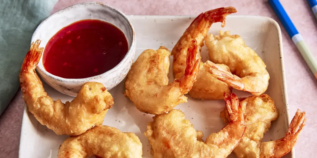 Knusprige tempura garnelen auf einem Teller mit süß-saurer Sauce und Stäbchen.