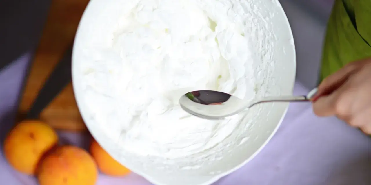 Eine Schüssel mit frisch geschlagener Sahne, bereit für ein Dessert. Ein Löffel ruht in der luftigen Masse.