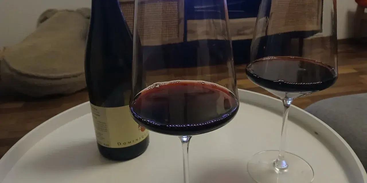 Zwei Gläser Rotwein und eine Flasche Wein, die an die Beaujolais-Region erinnert, stehen auf einem weißen Tablett.