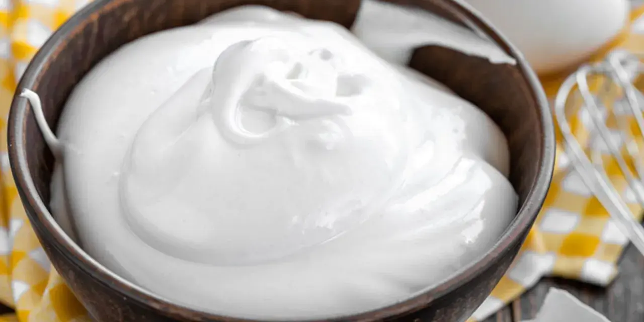 Perfekt geschlagener Eischnee in einer Schüssel, bereit für süße Kreationen. Daneben liegen Eier und ein Schneebesen.