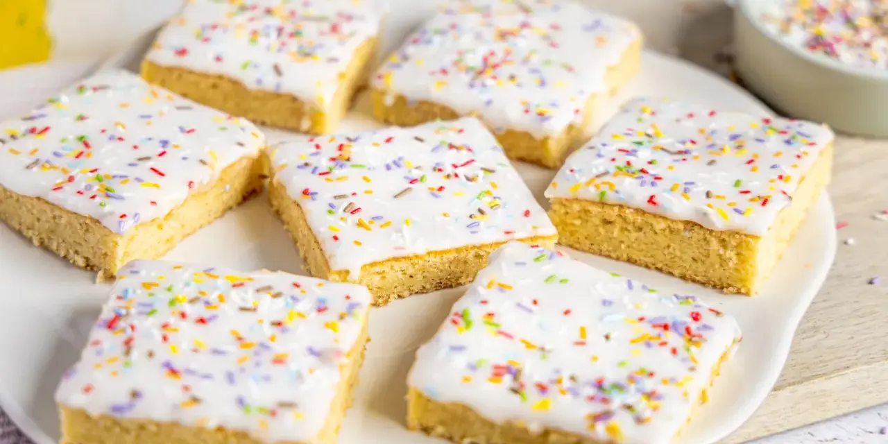 Sieben quadratische Kuchenstücke mit weißer Glasur und bunten Streuseln, perfekt für ein schnelles Fantakuchen Tassenrezept.