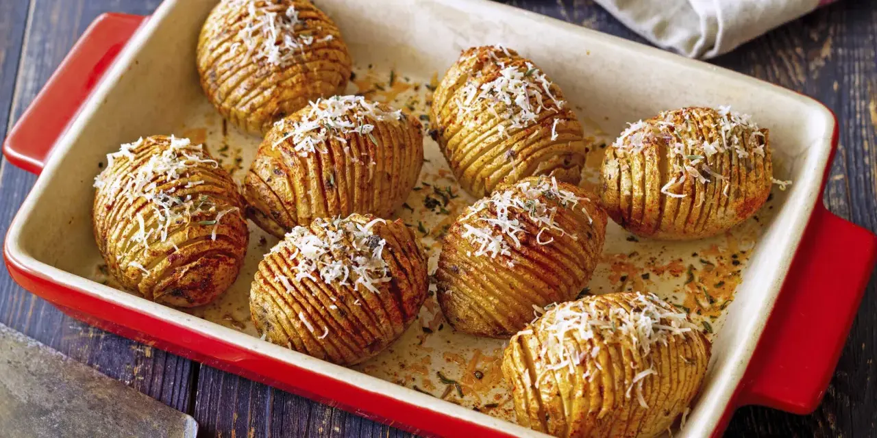 A red baking dish holds golden-brown hasselback kartoffeln, sprinkled with grated cheese and herbs.
