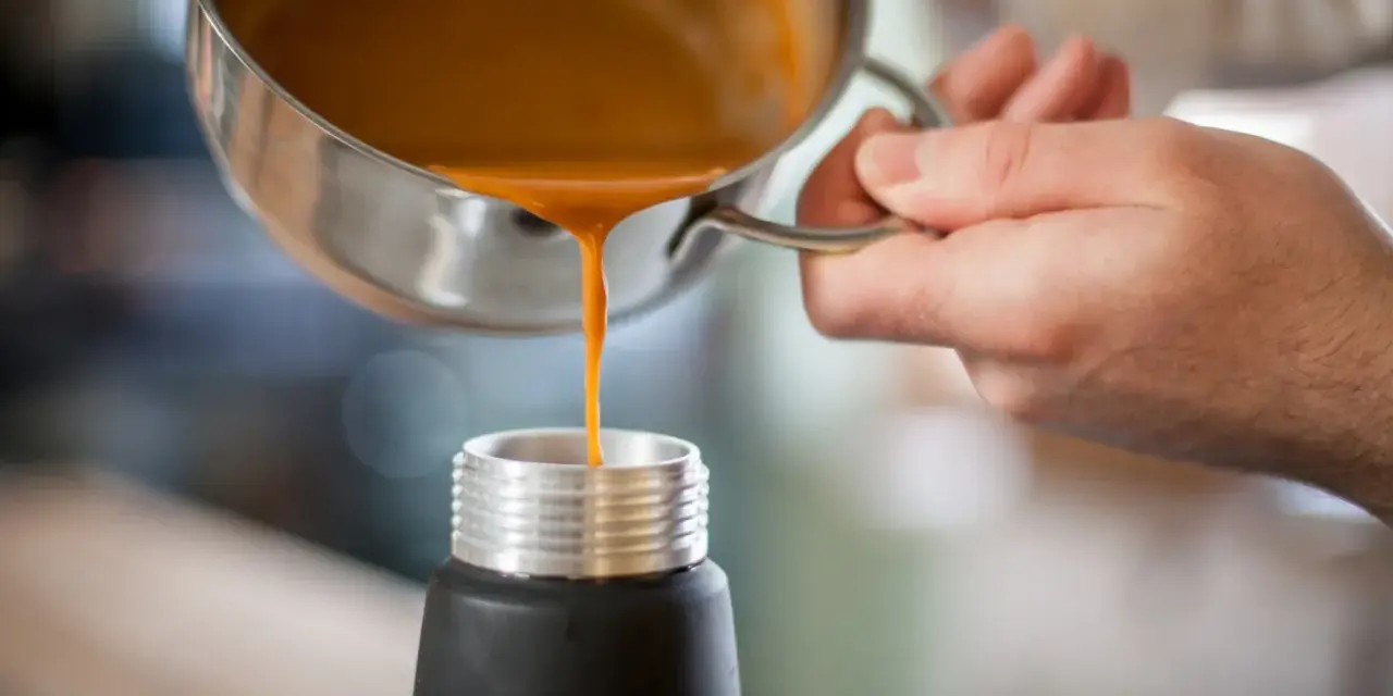 Eine orangefarbene Flüssigkeit wird aus einem Topf in ein schwarzes Gefäß gegossen. Ist das eine Espuma?
