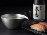 Sake-Flasche und eine Kanne mit Sake, die klassische Getränke, was trinkt man zu Sushi. Sushi-Stücke liegen daneben.