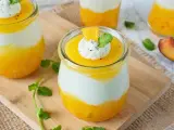 Erfrischendes Solero Dessert im Glas mit Mango-Fruchtsoße, weißer Creme und einem Klecks Sahne, garniert mit Minze und Orangenspalte.