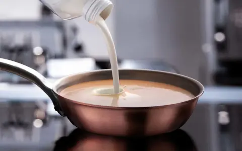 Sahne wird in eine Pfanne mit einer cremigen Sauce gegossen. Perfekt, welche Sahne zum Kochen für eine köstliche Mahlzeit.
