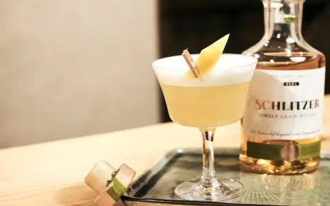 Ein erfrischender Sour Cocktail mit Zitronenspalte, neben einer Flasche Schlitzer Single Grain Whisky. Perfekt für ein Sour Cocktail Rezept.