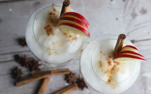 Zwei cremige Wintercocktails mit Zimt, Apfelscheiben und Sternanis.