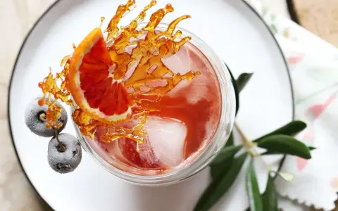 Ein erfrischender Sling Cocktail mit Blutorange, gefrorenen Beeren und Karamell-Dekoration.
