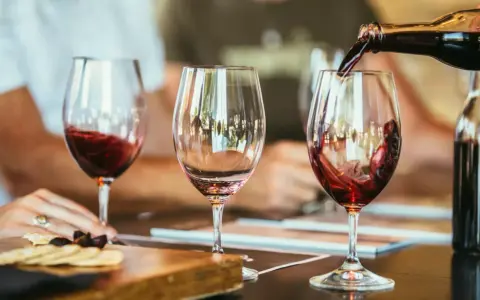 Rotwein wird in ein Glas gegossen, der Duft von **Wein** und **Tanninen** liegt in der Luft. Daneben ein leeres Glas und ein Teller mit Käse und Crackern.