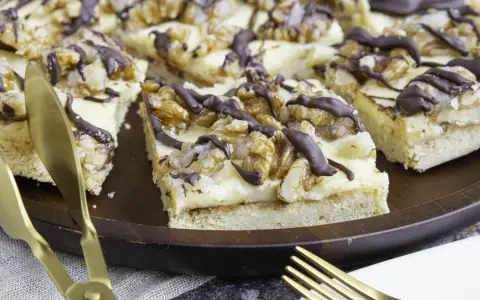 Ein "friss dich dumm kuchen" mit cremiger Füllung, Walnüssen und Schokoladendrizzle auf einem Holztablett. Goldene Gabeln liegen bereit.
