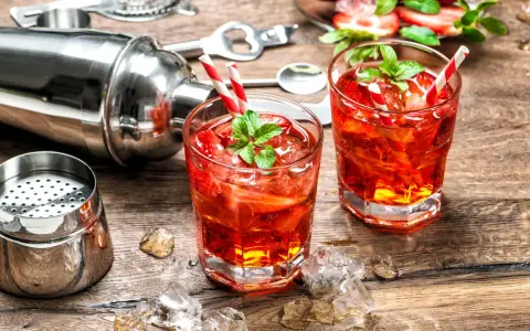 Zwei erfrischende Cocktails mit Erdbeeren und Minze, bereit zum Genießen. Dazu ein Shaker und Eiswürfel auf Holztisch. Perfekt für gute Cocktails.