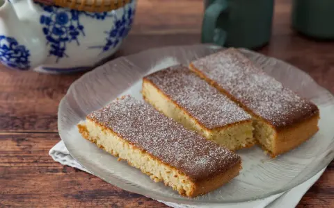 Drei rechteckige Stücke mandelkuchen vom blech, mit Puderzucker bestäubt, auf einem Glas-Teller.