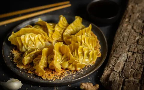 Goldbraune Gyoza auf knusprigem Sesam-Bett, bereit für ein köstliches Dumplings-Rezept. Dazu Sojasauce und Ingwer.