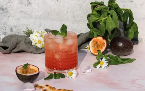 Erfrischender sanbitter cocktail mit Passionsfrucht, Minze und Eiswürfeln, garniert mit Gänseblümchen.