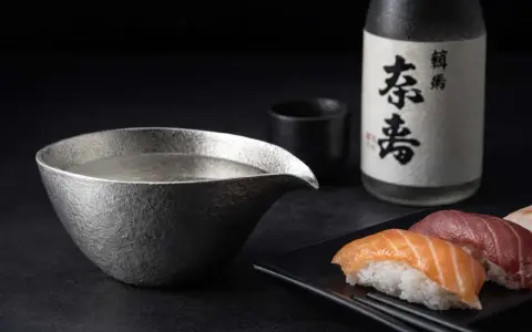 Sake-Flasche und eine Kanne mit Sake, die klassische Getränke, was trinkt man zu Sushi. Sushi-Stücke liegen daneben.
