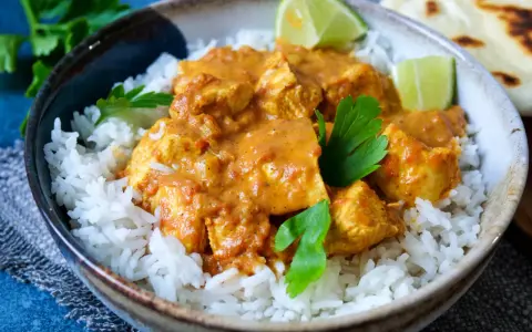 Ein köstliches indisches Curry mit zarten Hähnchenstücken in cremiger Sauce, serviert auf lockerem Reis, garniert mit frischer Petersilie und Limettenspalten.