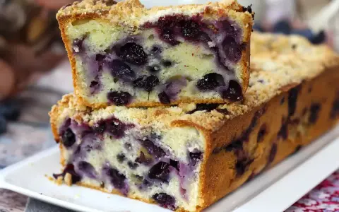 Saftiger Blaubeerkuchen mit Streuseln, ein Stück gestapelt auf dem ganzen Kuchen.