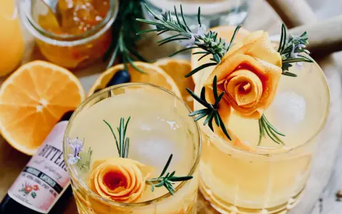 Zwei erfrischende Cocktails mit Orangenscheiben, Rosmarin und einer Orangenschalenrose. Daneben eine Flasche "Bitters" mit Lavendelgeschmack.