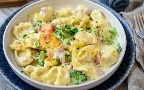 Ein cremiger Tortellini Auflauf mit Brokkoli und Schinken, überbacken mit Käse und bestreut mit Petersilie.