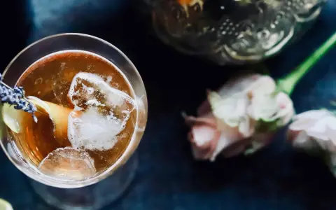 Ein erfrischender Gin Tee mit Eis, Zitrone und Lavendelblüten. Daneben zarte Rosen und eine verzierte Karaffe.