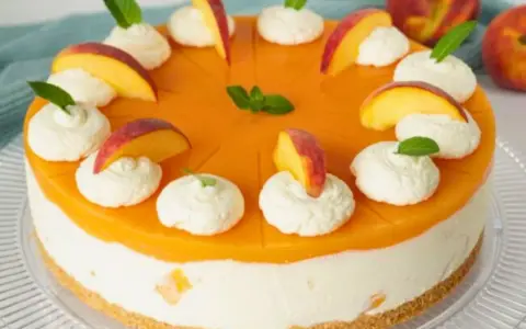 Eine Maracuja Torte mit Pfirsichstücken und Sahnetupfern, verziert mit Minze.
