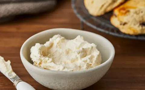 Cremiger Aufstrich in einer Schale, bereit für das perfekte Scones Rezept. Daneben ein Messer mit etwas Aufstrich.