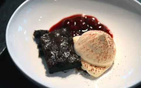 Schokoladenbrownie mit Fruchtsauce und einer perfekt hergestellten, luftigen Espuma, bestäubt mit Kakao.