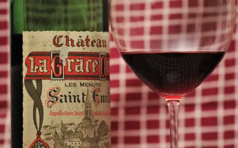 Ein Glas Rotwein neben einer Flasche Château La Grace Dieu. Die Bedeutung von "Grand Cru" auf dem Etikett deutet auf höchste Qualität hin.
