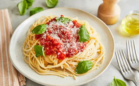 Ein Teller Spaghetti Napoli mit Tomatensauce, Parmesan und frischem Basilikum.