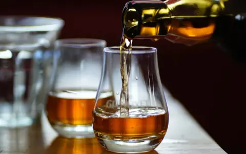 Bernsteinfarbener schottischer Whisky fließt aus einer Flasche in ein Glas. Die schottischer Whisky sorten alphabetisch zu verkosten ist ein Genuss.