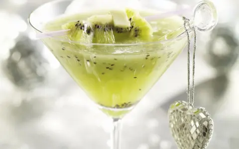 Erfrischender Kiwi-Cocktail im Martiniglas, garniert mit frischen Kiwischeiben und einem glitzernden Herz-Anhänger.