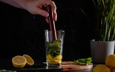 Ein Barkeeper bereitet einen erfrischenden Cocktail mit Basilikum und Gin zu, indem er die Zutaten im Glas zerdrückt.