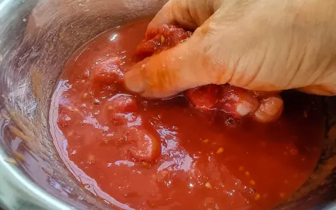 Hand zerdrückt Tomaten in einer Schüssel. So einfach lässt sich Tomatensauce selber machen.