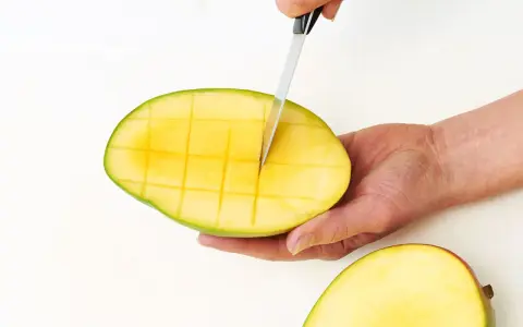 Eine Hand schneidet mit einem Messer eine reife Mango in Würfel. So einfach lässt sich die Frucht für den Verzehr vorbereiten.