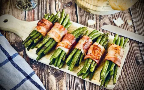 Leckeres Speckbohnen Rezept: Grüne Bohnen umwickelt mit knusprigem Speck, serviert auf einem Holzbrett.