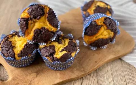 Zupfkuchen Muffins mit Marmormuster aus dunklem Schoko- und hellem Teig in blauen Papierförmchen auf einem Holzbrett.
