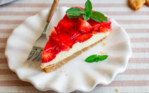 Ein Stück einfache Torte mit Erdbeeren und Minze auf einem weißen Teller.