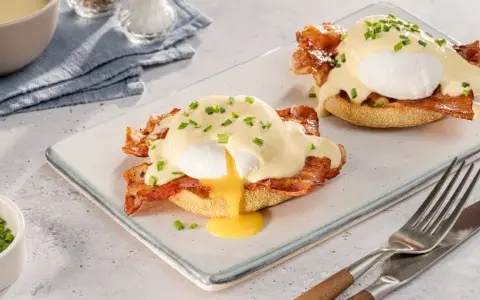 Zwei köstliche Eggs Benedict auf einem Teller, mit flüssigem Eigelb und garniert mit Schnittlauch.