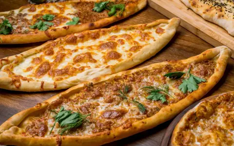 Mehrere Pide-Gerichte, darunter eines mit Käse und eines mit Hackfleisch, sind auf einem Holztisch arrangiert. Ein köstliches Pide Rezept!
